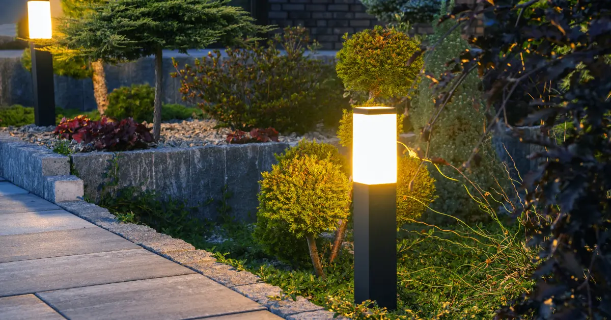 Modern outdoor landscape lights illuminating a garden walkway, highlighting shrubs and greenery at dusk.