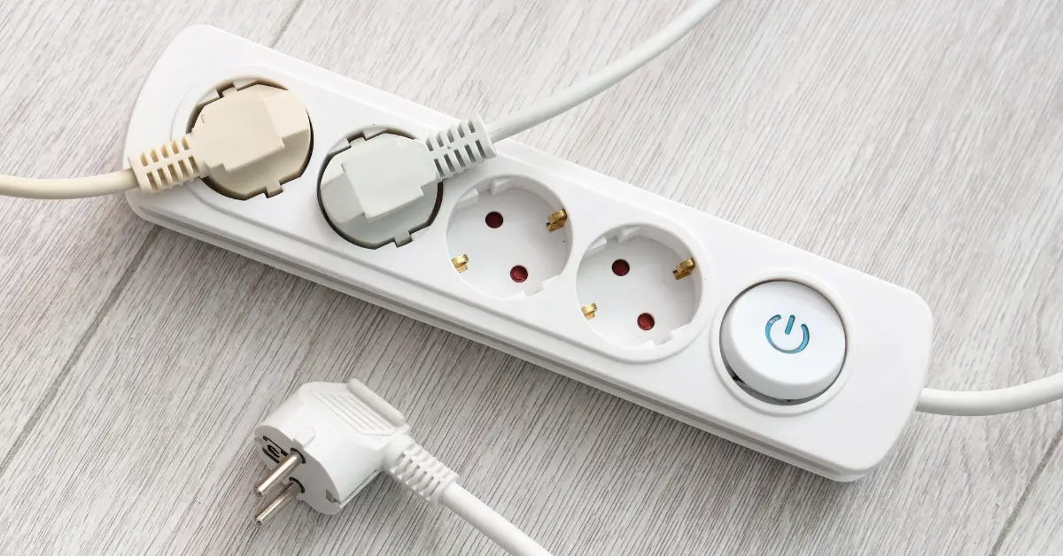 Power strip with multiple plugs inserted and empty outlets visible, placed on a light wood surface to illustrate safe electrical usage.